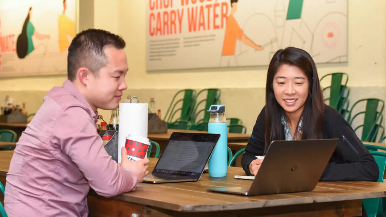 a man and a woman sitting at a table with laptops