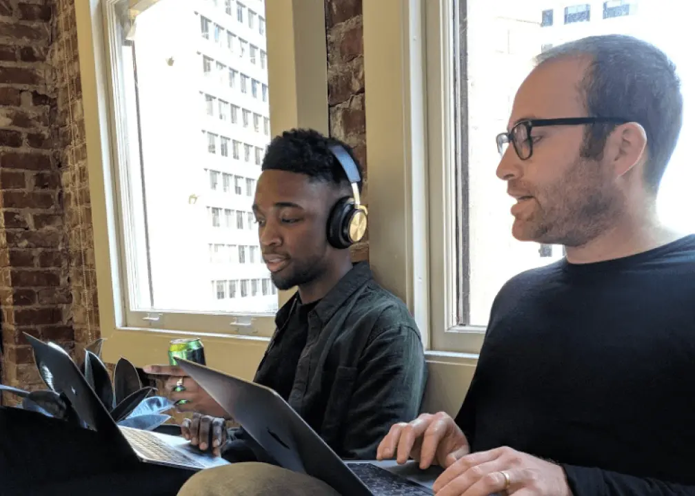 a couple of men sitting next to each other on laptops